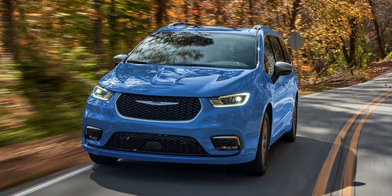 Blue Chrysler Pacifica minivan driving on a winding autumn road