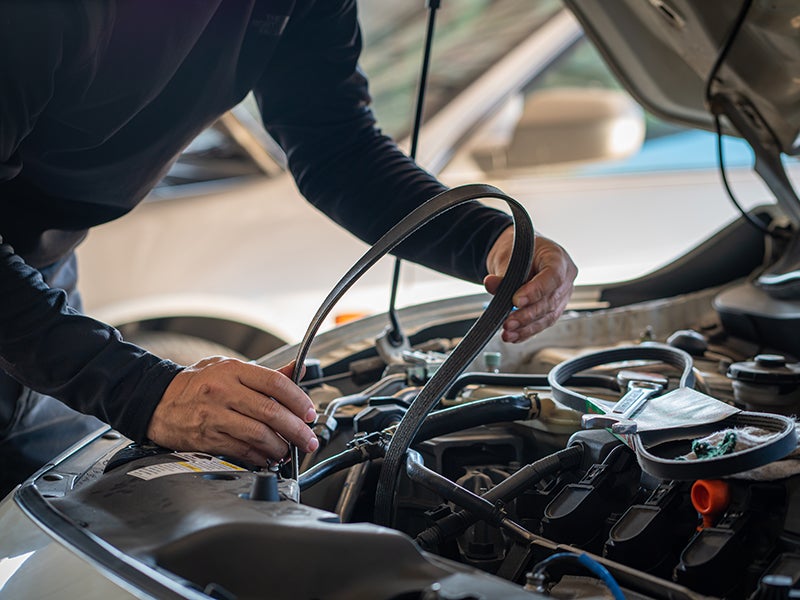 Mechanic installing a new drive belt in a car engine with the hood open.