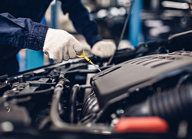 A gloved hand inserting a yellow dipstick into a car engine to check the oil level.