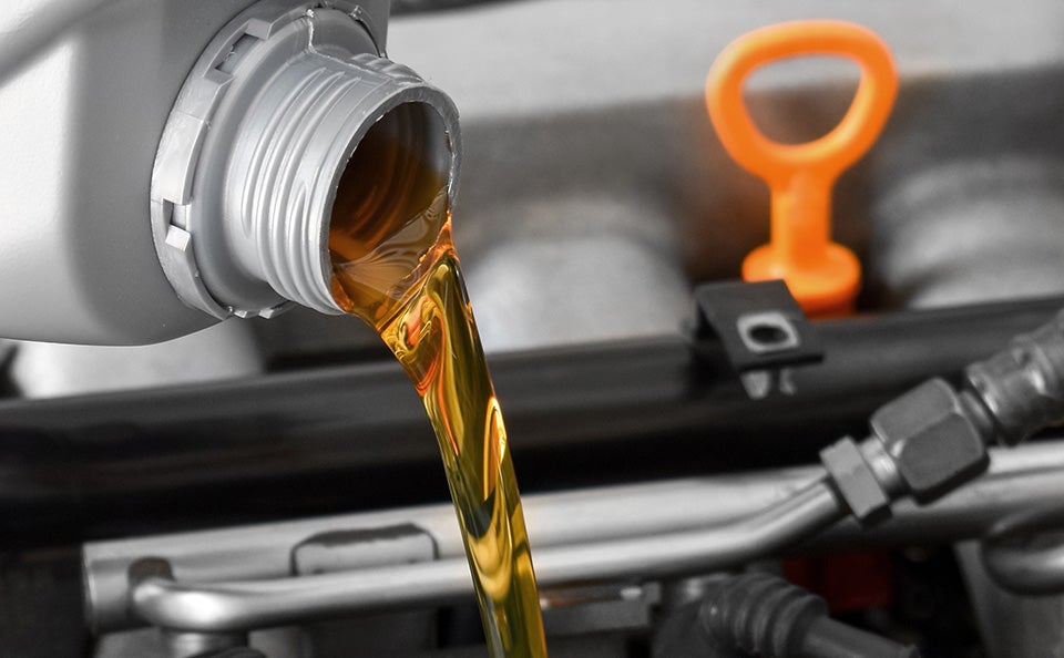 Fresh golden motor oil being poured into a car engine during routine maintenance.